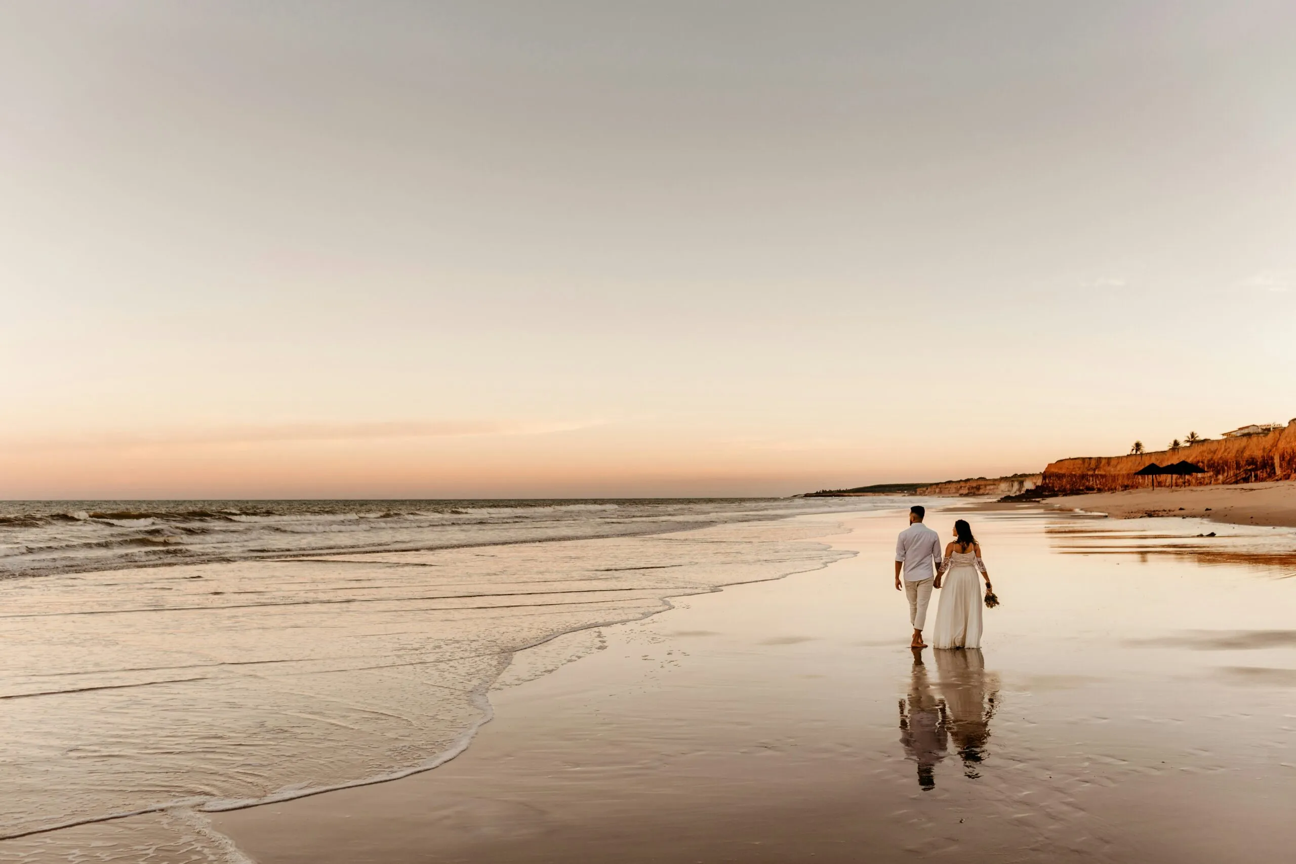 Couple walking along beach at sunset on wedding day.