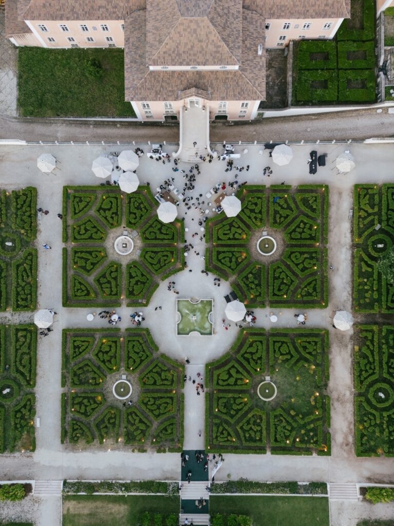 Aerial view of wedding guests gathering in the formal gardens of a pink palace in Portugal