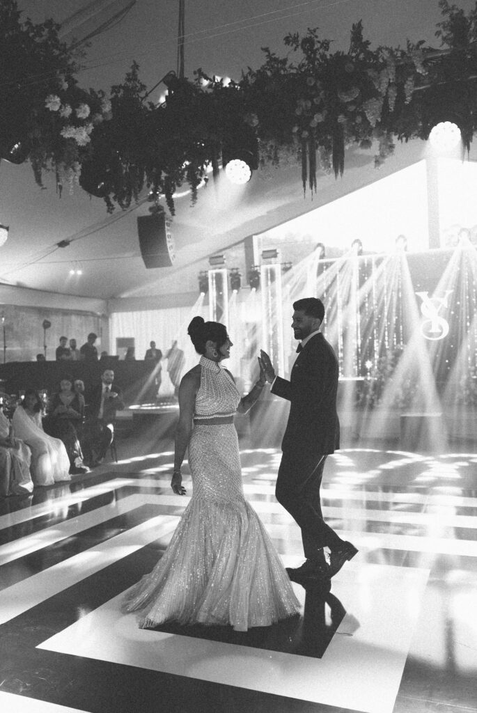 Black and white photo of a couple’s first dance under hanging florals and stage lighting in a marquee in Portugal