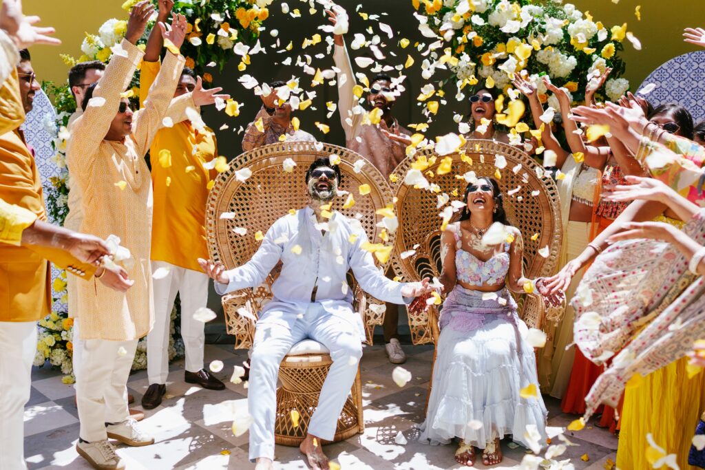 Couple laughing as guests shower them with yellow and white petals at a haldi ceremony in Portugal