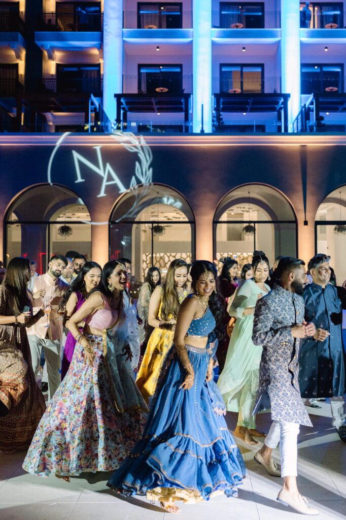 Guests in colourful lehengas and sherwanis dancing outside a lit-up resort hotel in Greece