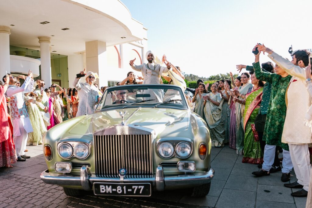 Groom arriving in a vintage convertible for his baraat, surrounded by dancing guests in Portugal