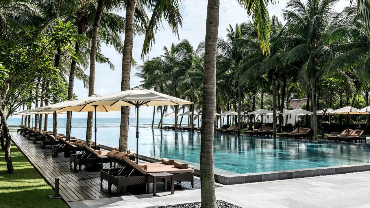 Luxury pool with lounge chairs with umbrellas and view of coastline/sea