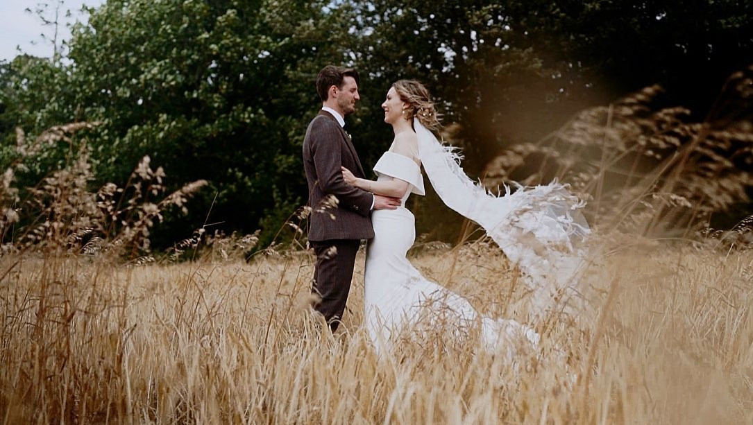 Bride and groom pose in a field for their wedding video